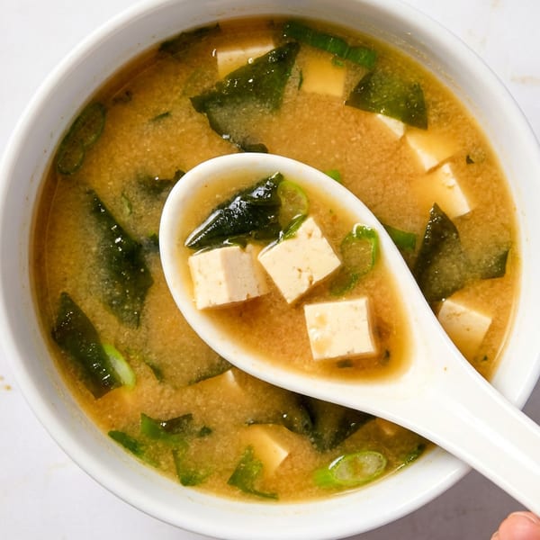 Overhead view of miso soup with tofu, seaweed, and scallions in a white bowl, with a spoon lifting some.