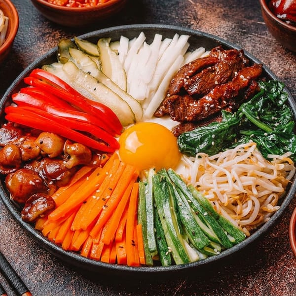 Colorful Korean bibimbap bowl with beef, vegetables, and egg yolk, with chopsticks and side dishes.
