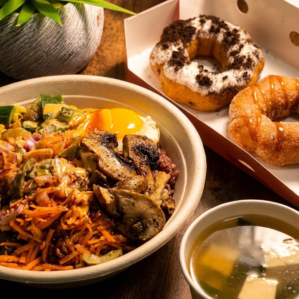 A colorful poke bowl with an egg, soup, and a box of assorted donuts on a wooden table.