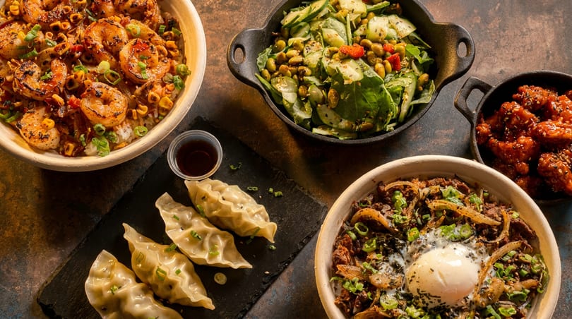 An overhead view of various Asian dishes, including shrimp, dumplings, salad, and a rice bowl.