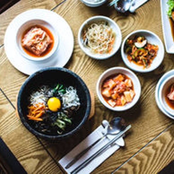 Overhead view of a Korean meal with bibimbap, kimchi, and various banchan on a wooden table.