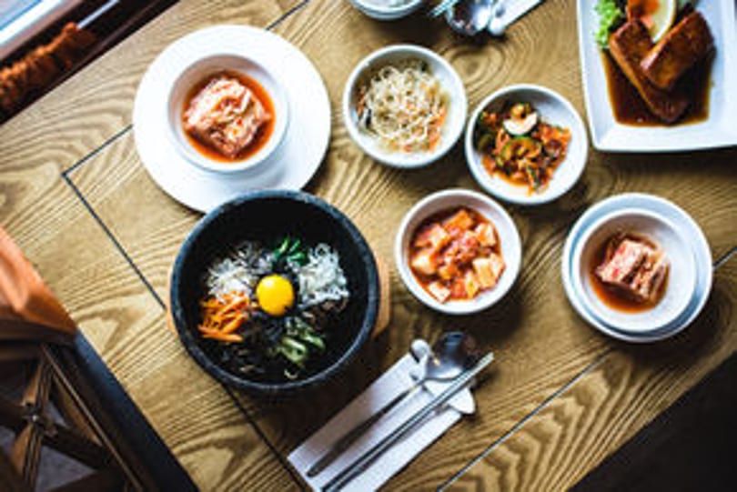 Overhead view of a Korean meal with bibimbap, kimchi, and various side dishes on a wooden table.