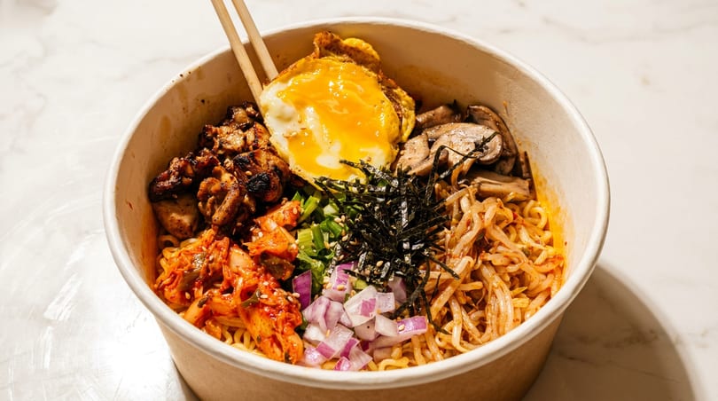 A Korean ramen bowl with kimchi, grilled chicken, fried egg, mushrooms, and bean sprouts.